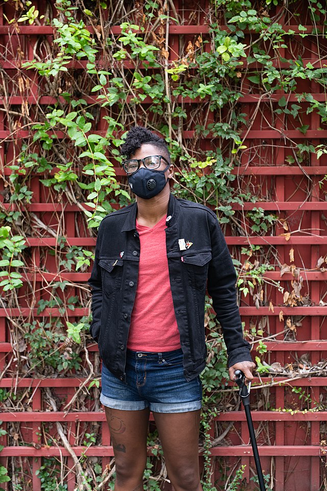 Black woman who is a cane user wearing a face mask in a garden